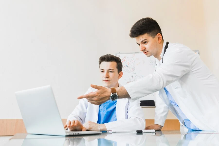 A doctors discuss with medical biller about medical billing and coding on a laptop.