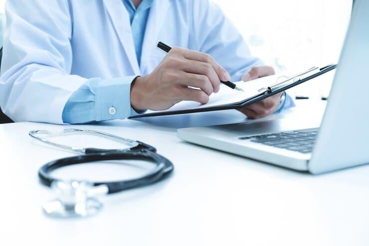 Doctor reviewing paperwork with patient in background inhaler on desk.