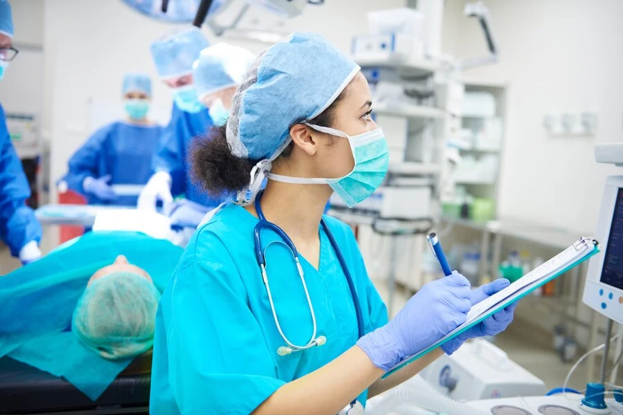 A woman in medical scrubs and a mask writing on a clipboard about Surgery medical Billing Services.